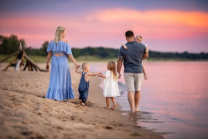 Family of five walks along the beach. The sky is pink and purple.